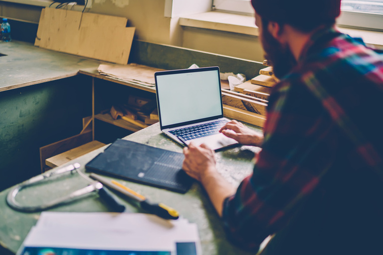 Anonymous repairman in casual shirt chatting on laptop at workshop